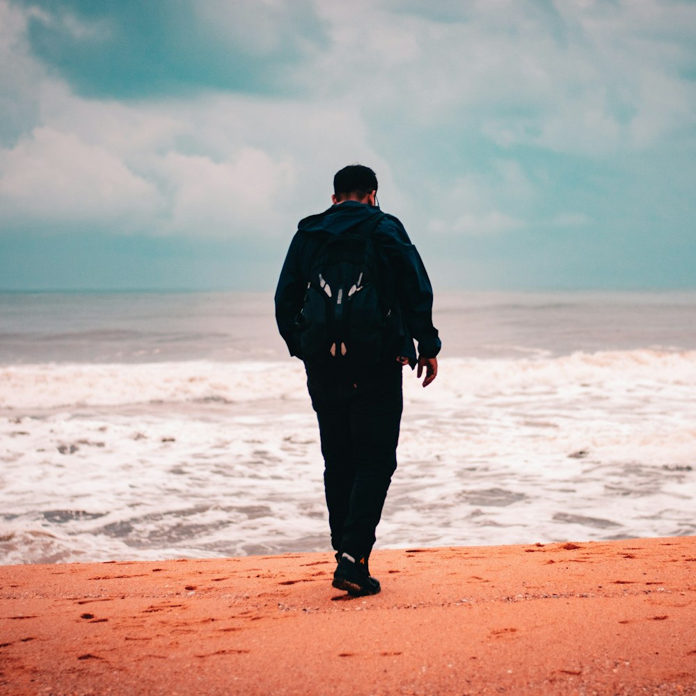 man in black jacket standing on brown sand near sea during daytime