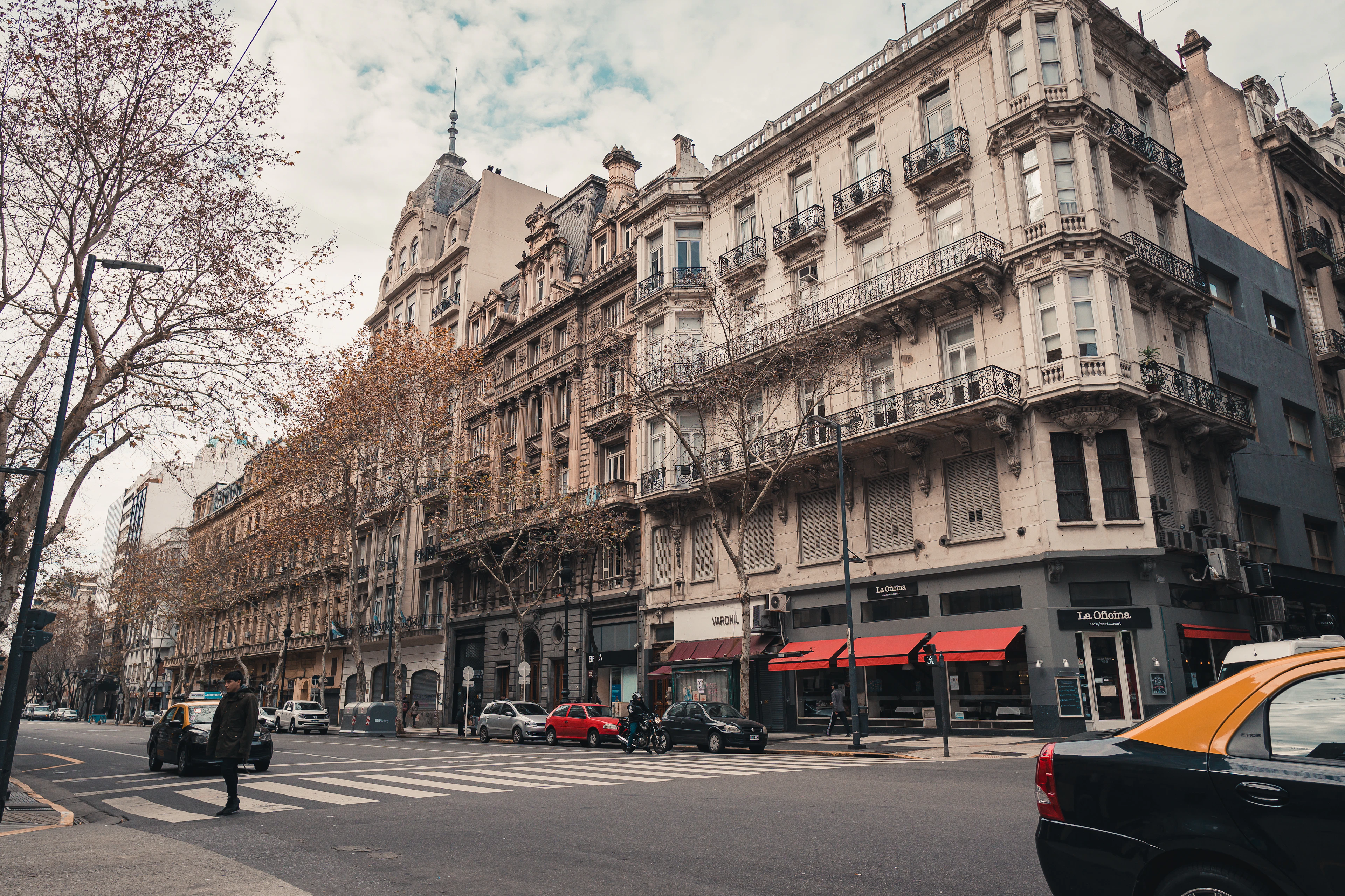Ornate Beaux-Arts apartment buildings line a wide Buenos Aires avenue with a black taxi and autumn trees below.