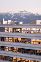 A sleek downtown Denver office building glowing at sunset with mountain peaks in the background.