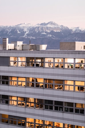 A sleek downtown Denver office building glowing at sunset with mountain peaks in the background.