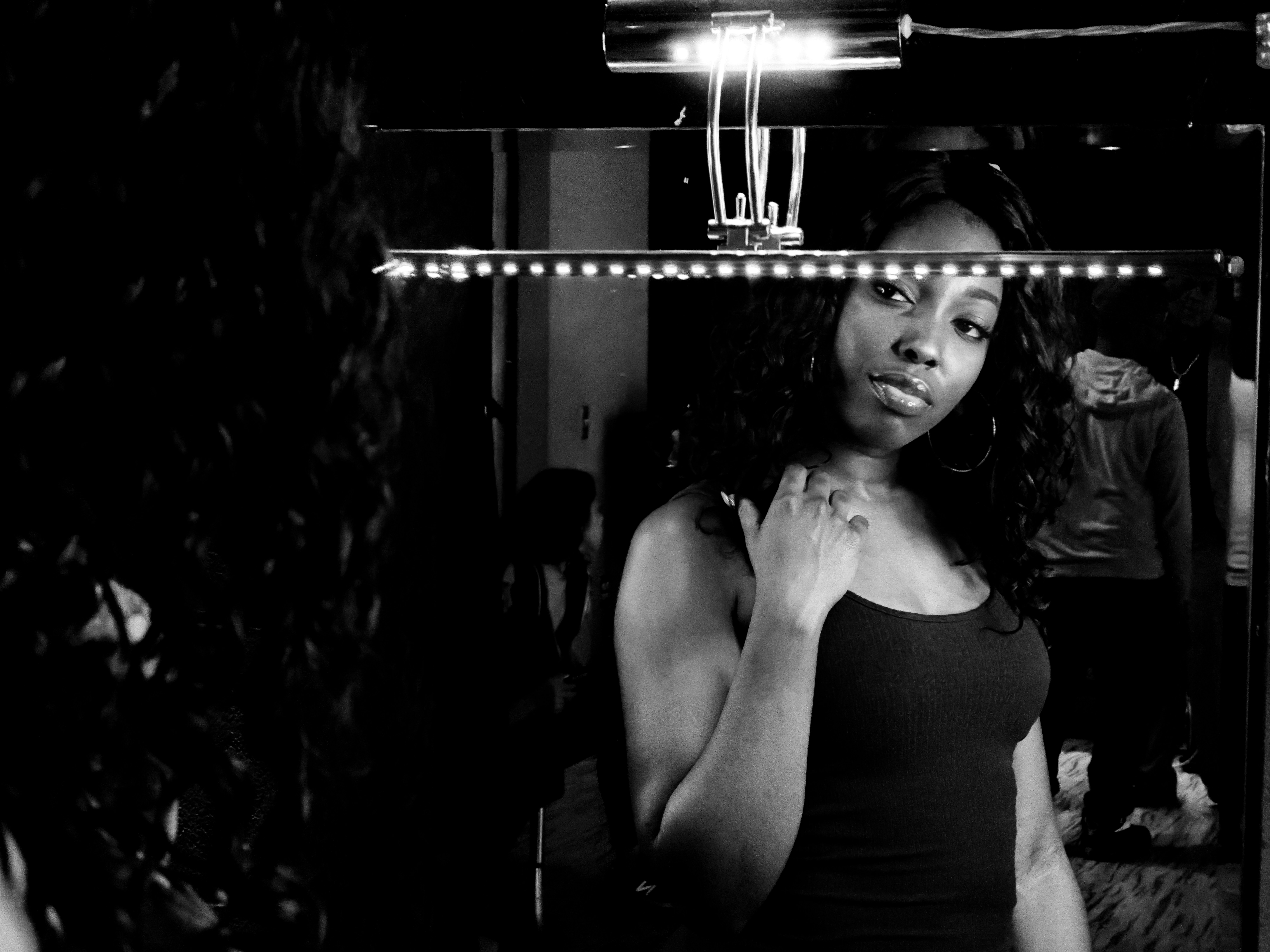 woman in black tank top, A woman looks at herself in the mirror as she prepares to star in a music video. 