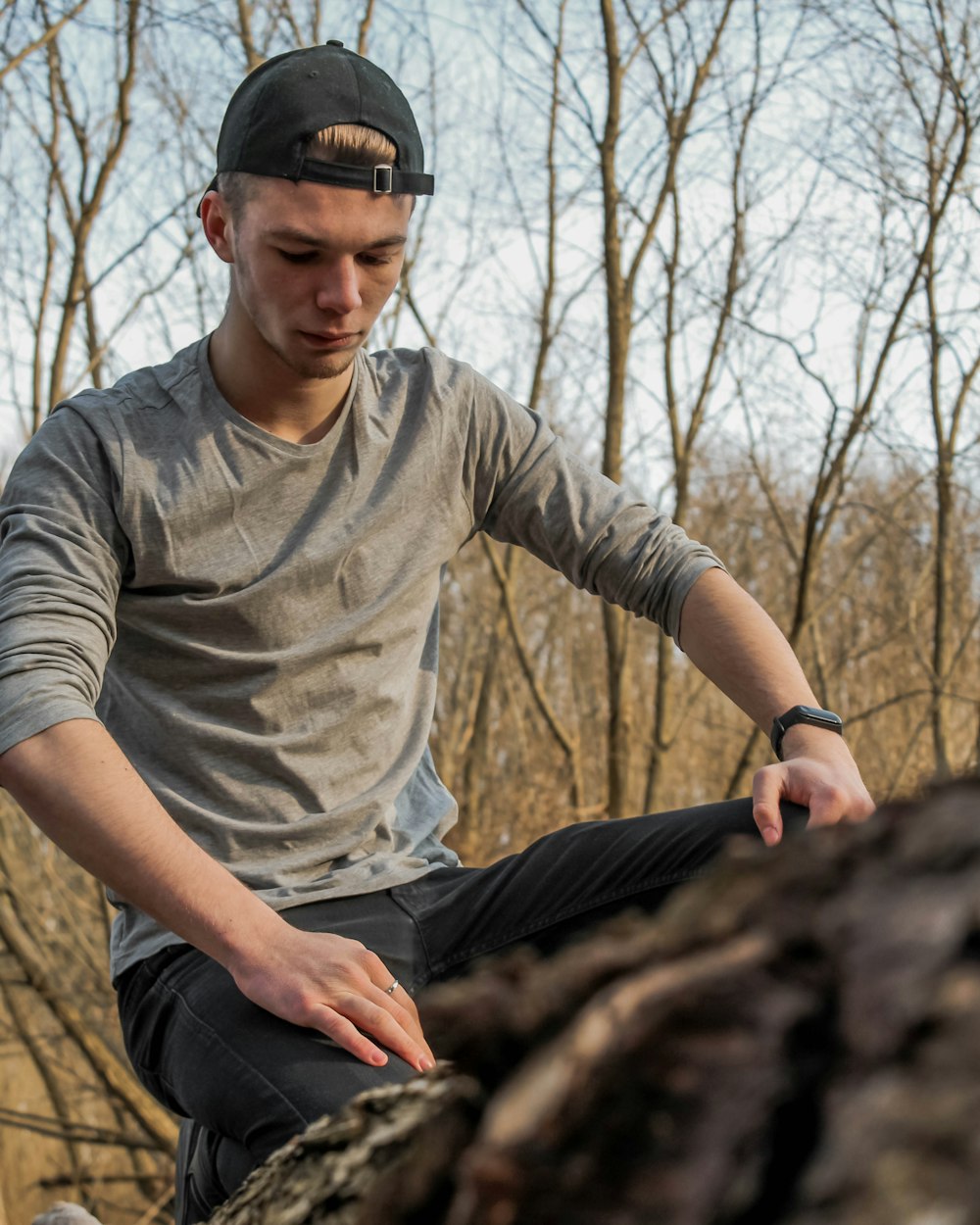 man in grey crew neck t-shirt and blue denim jeans sitting on brown tree log