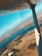 An aerial view of a landscape featuring a large body of water surrounded by fields and scattered buildings. The wing of an aircraft is visible in the foreground, indicating the photo was taken from within a plane. The sky is clear and blue, suggesting fair weather.