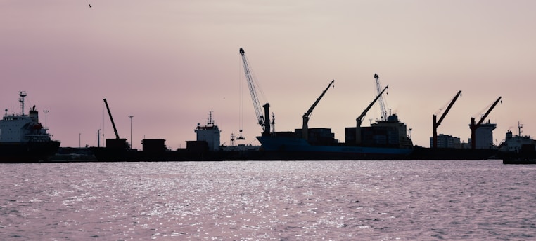 A serene seaport at dawn with cargo ships and cranes silhouetted against the rising sun, symbolizing sustainable logistics.