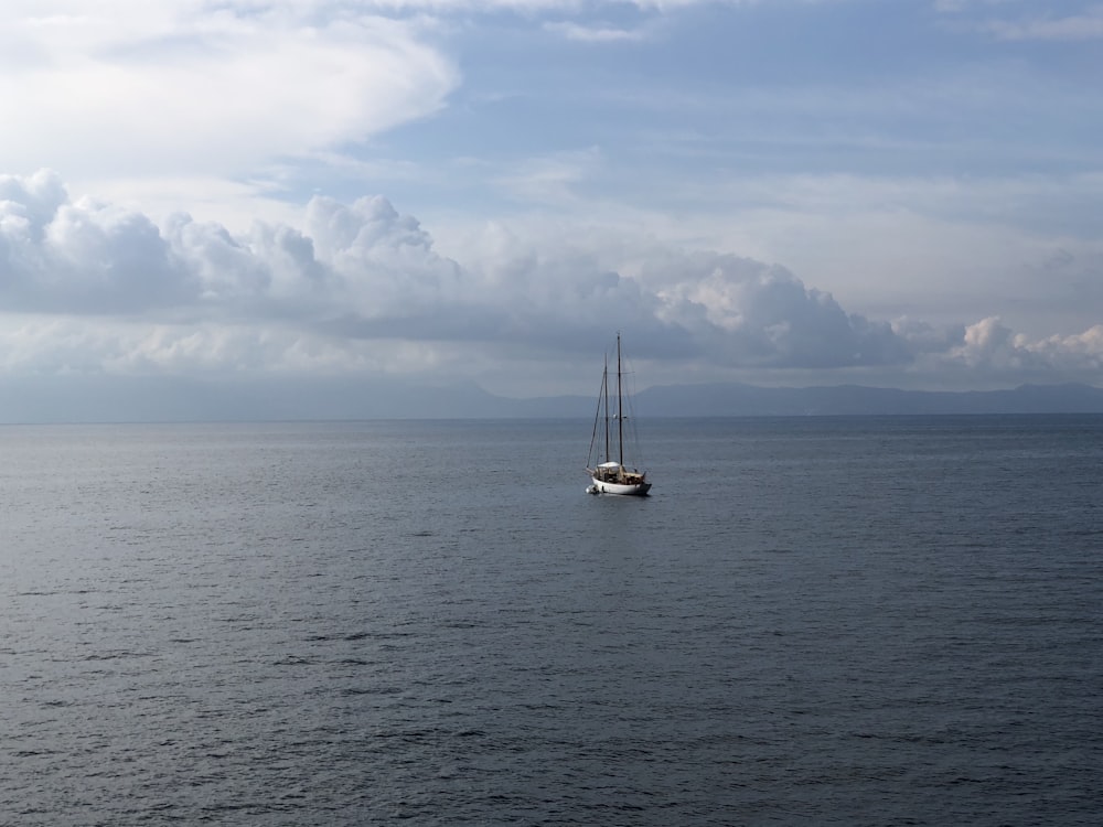 white sailboat on sea under white clouds and blue sky during daytime