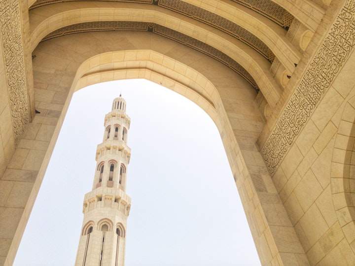 Photo of a minaret being seeing from the arch of a mosque.