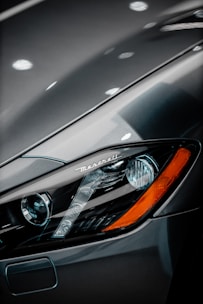 Close-up view of a luxury car's headlight, featuring sleek and modern design elements. The brand name is visible above the headlight, with a polished metallic surface reflecting light.