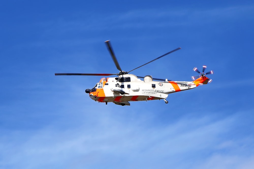 helicóptero laranja e branco voando sob o céu azul durante o dia