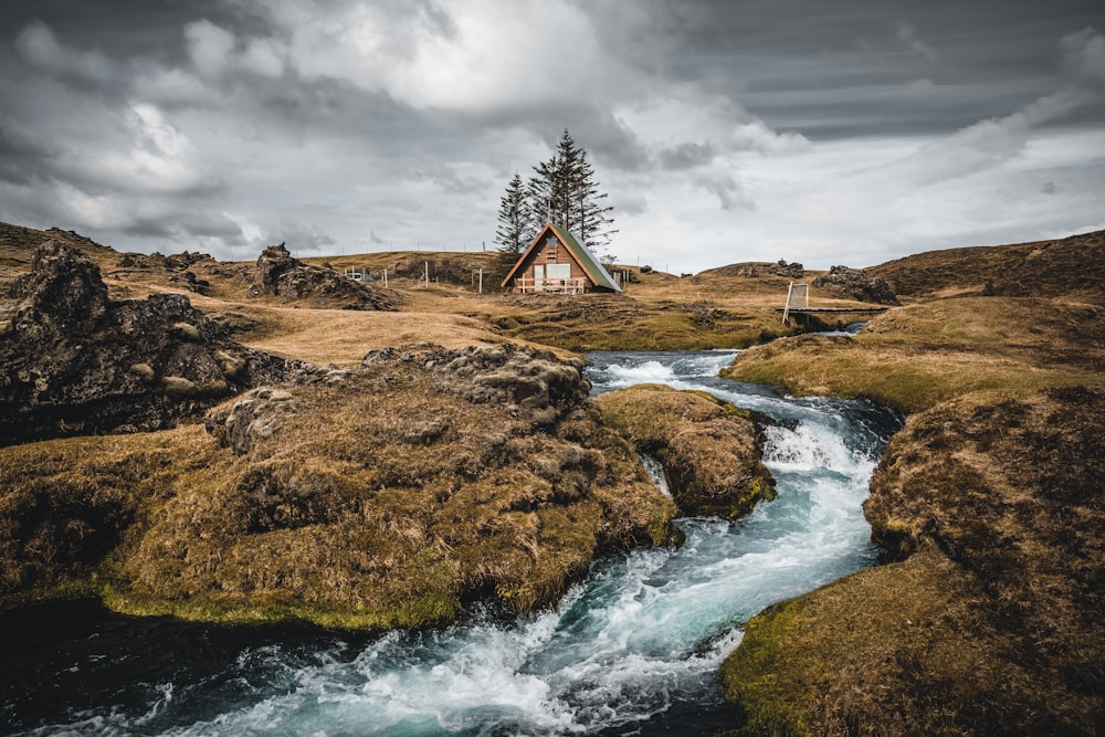 brown wooden house on brown rock formation near body of water under gray clouds