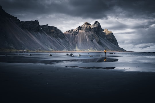 person in yellow jacket standing on snow covered ground near snow covered mountain during daytime in Stokksnes Iceland