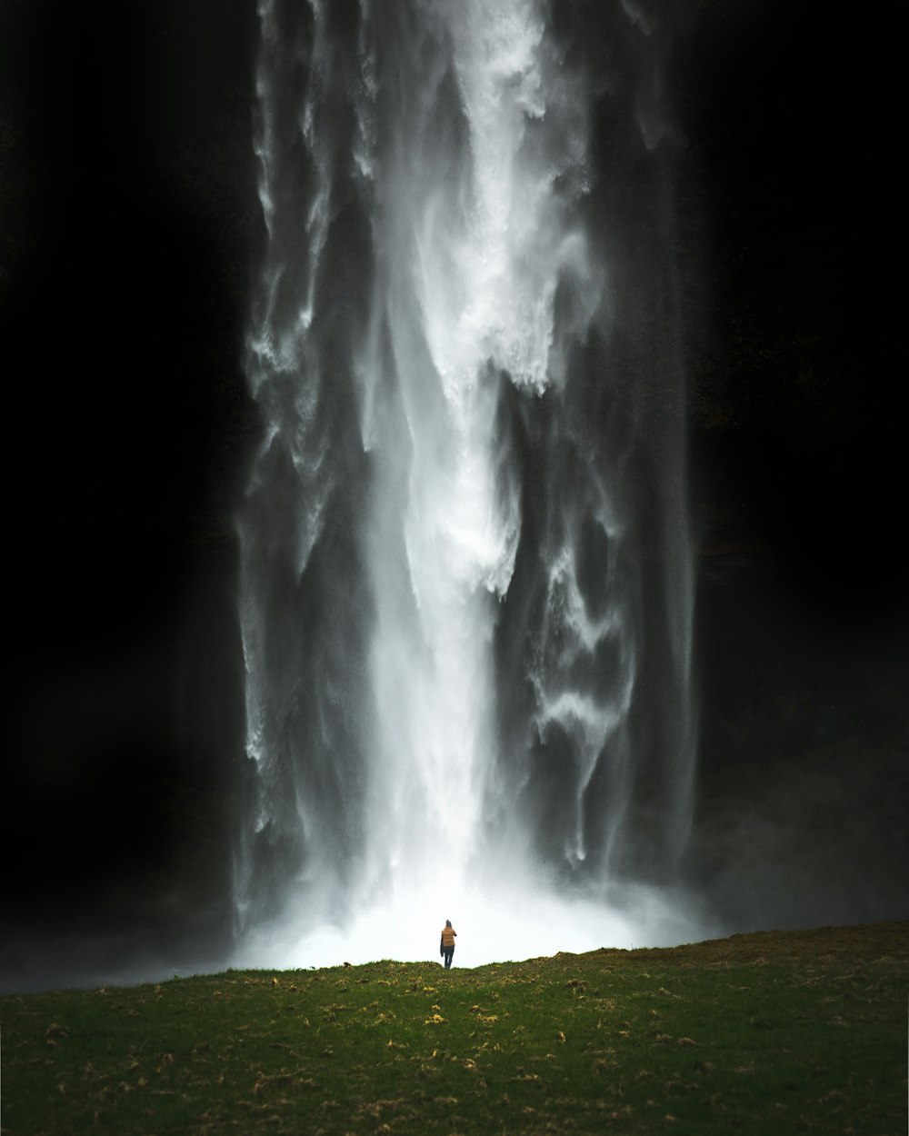 person standing on green grass field near waterfalls during daytime