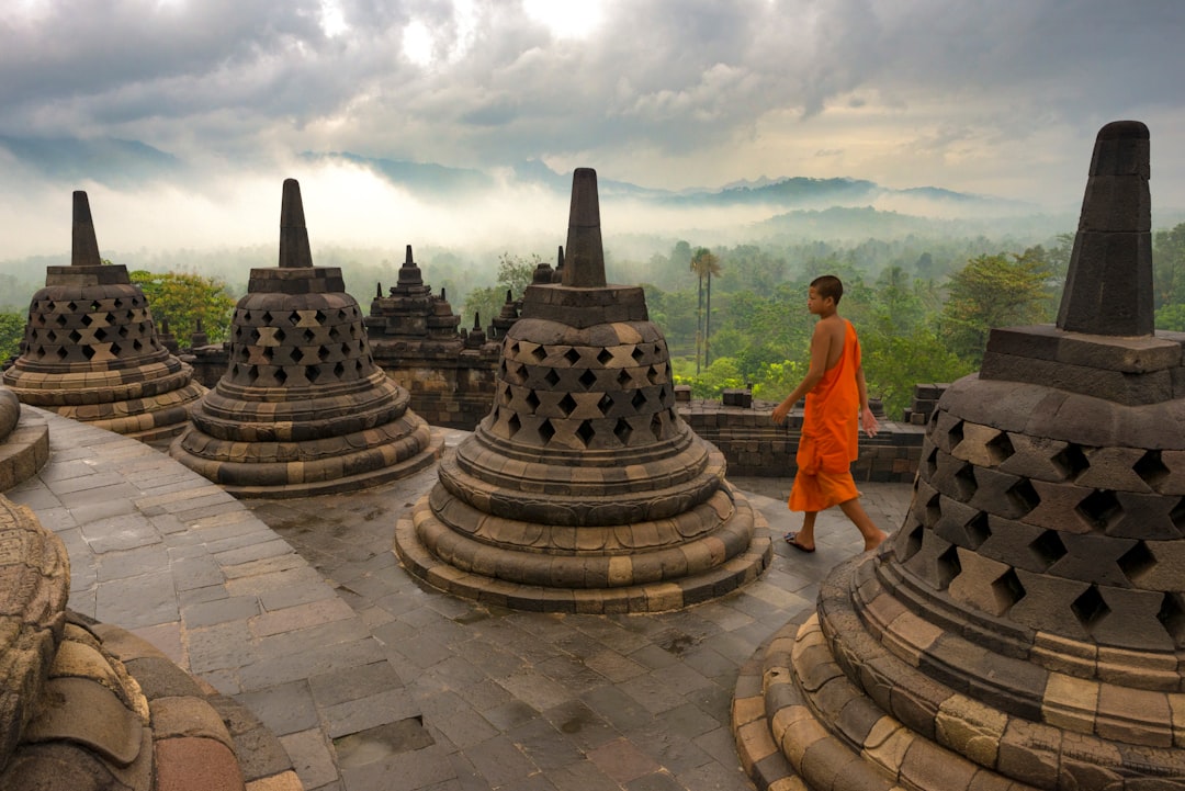 man in orange shirt standing near gold buddha statue