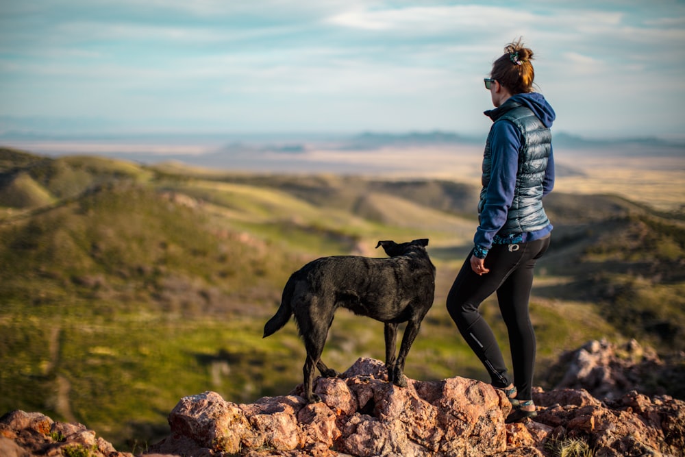 woman in blue denim jacket and black pants standing on brown rock beside black short coated