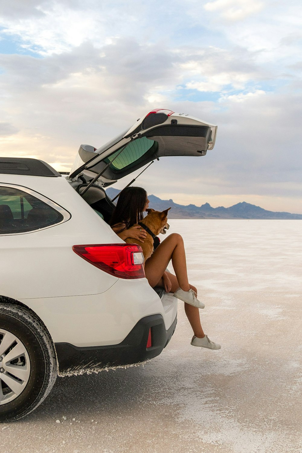 femme en débardeur rouge assise sur le capot de voiture blanc pendant la journée