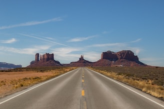 gray concrete road between brown mountains under blue sky during daytime