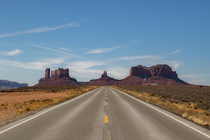 gray concrete road between brown mountains under blue sky during daytime