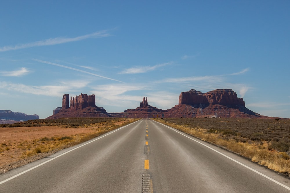 gray concrete road between brown mountains under blue sky during daytime