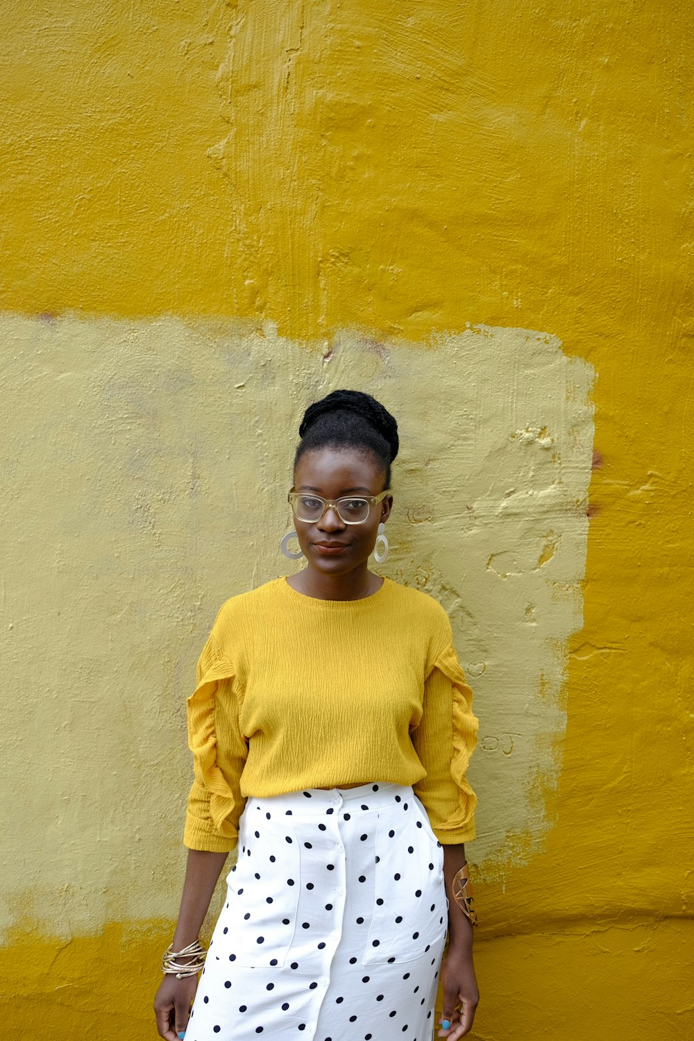 woman in yellow crew neck long sleeve shirt leaning on yellow painted wall
