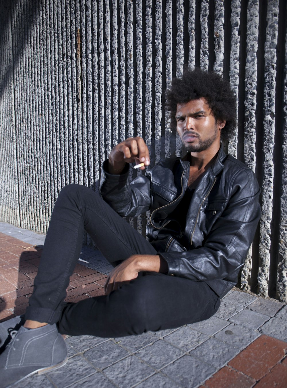 茶色の木製のベンチに座る黒い革のジャケットと黒いズボンの男