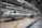 An assembly line in a car manufacturing plant with several partially assembled vehicle frames lined up. Robotic equipment and wiring are visible, emphasizing the mechanical aspect of the production process. The environment is clean and organized, with bright overhead lighting illuminating the industrial setting.