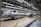An assembly line in a car manufacturing plant with several partially assembled vehicle frames lined up. Robotic equipment and wiring are visible, emphasizing the mechanical aspect of the production process. The environment is clean and organized, with bright overhead lighting illuminating the industrial setting.