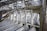 Multiple car doors and frames are lined up in a row inside an industrial facility with a high ceiling featuring metal beams and structures.