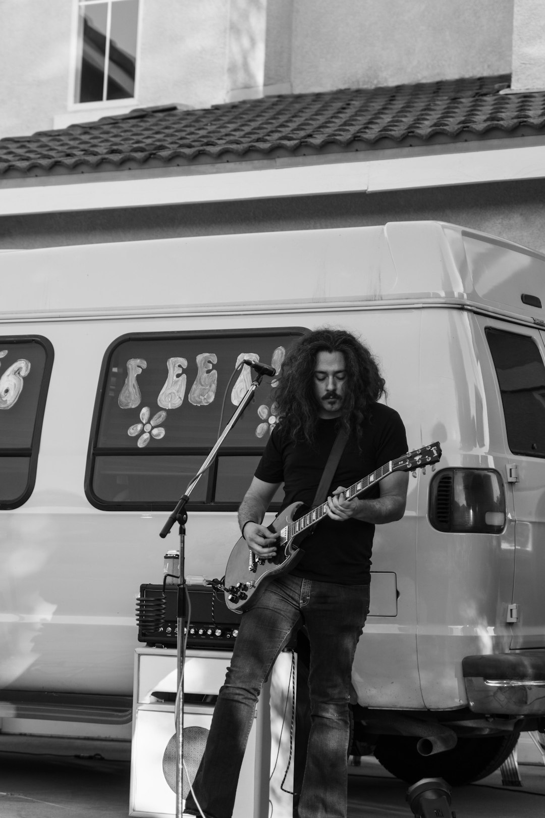 grayscale photo of woman in black shirt and denim jeans playing guitar