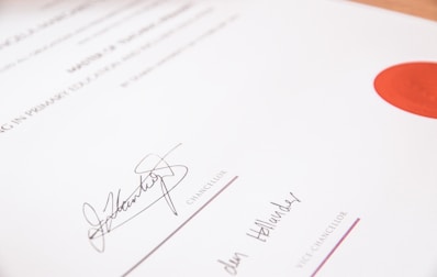 A close-up view of a formal document featuring signatures from a chancellor and a vice chancellor. The document has a clean layout, with printed text and a prominent red seal on the upper right side.