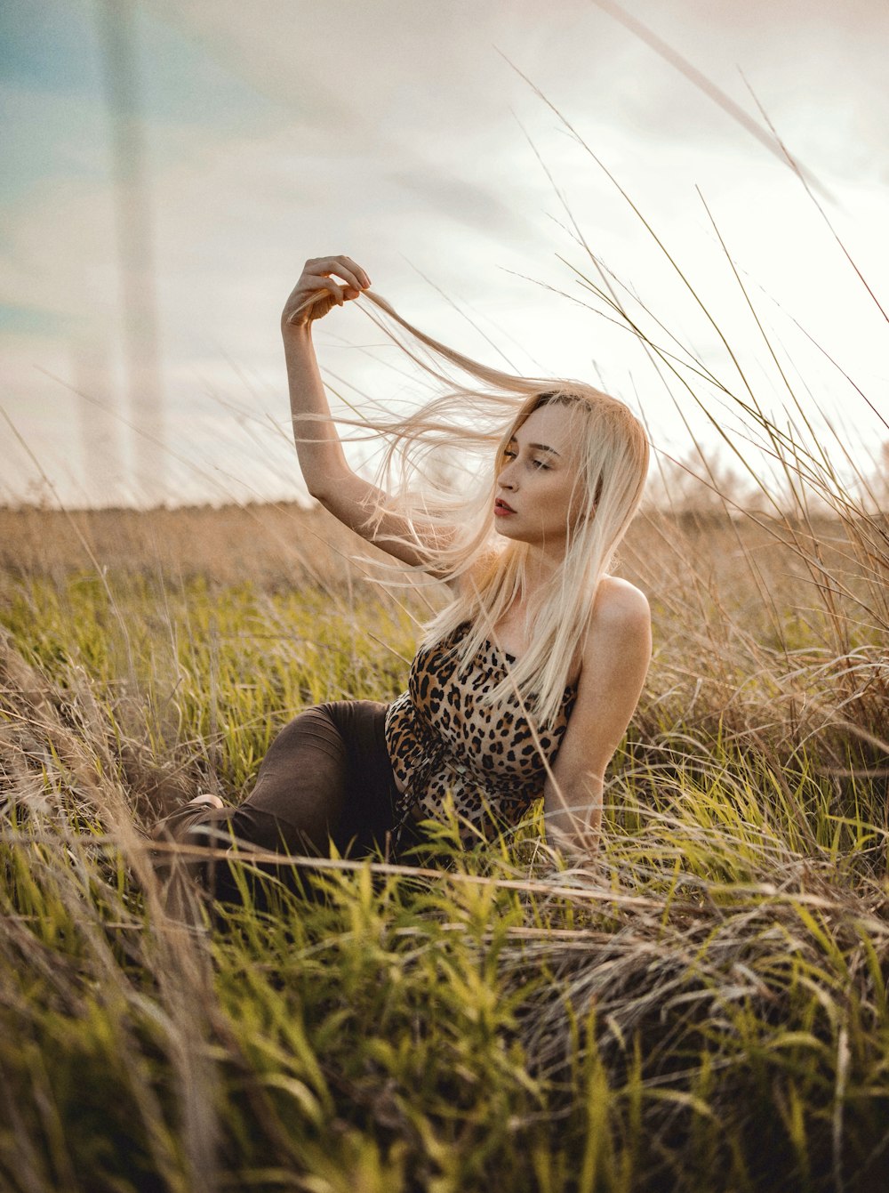 woman in black and white leopard print tank top sitting on green grass field during daytime