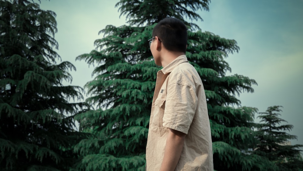 man in brown dress shirt standing near green tree during daytime