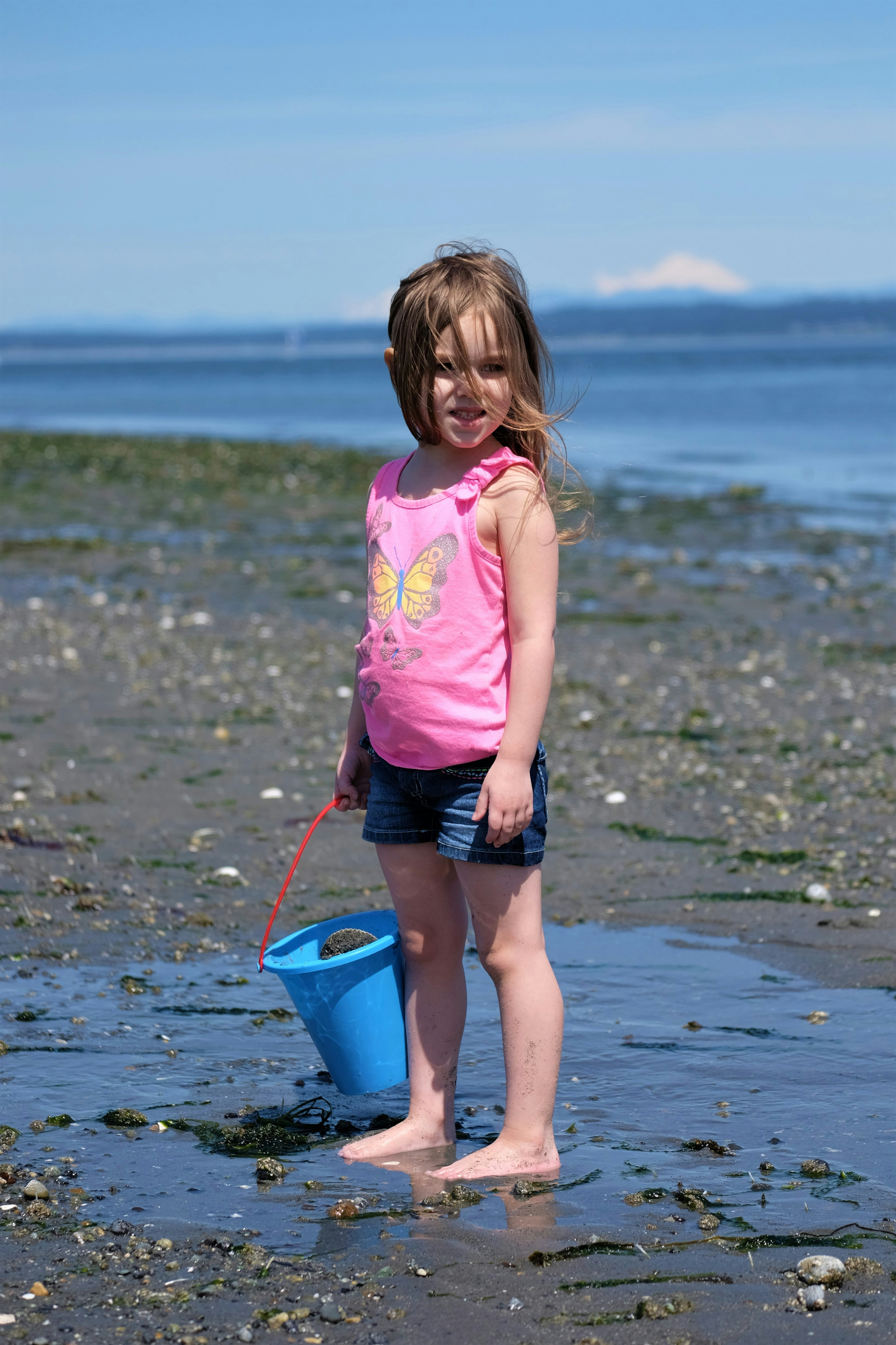 girl in pink shirt and black shorts standing on beach shore during daytime
