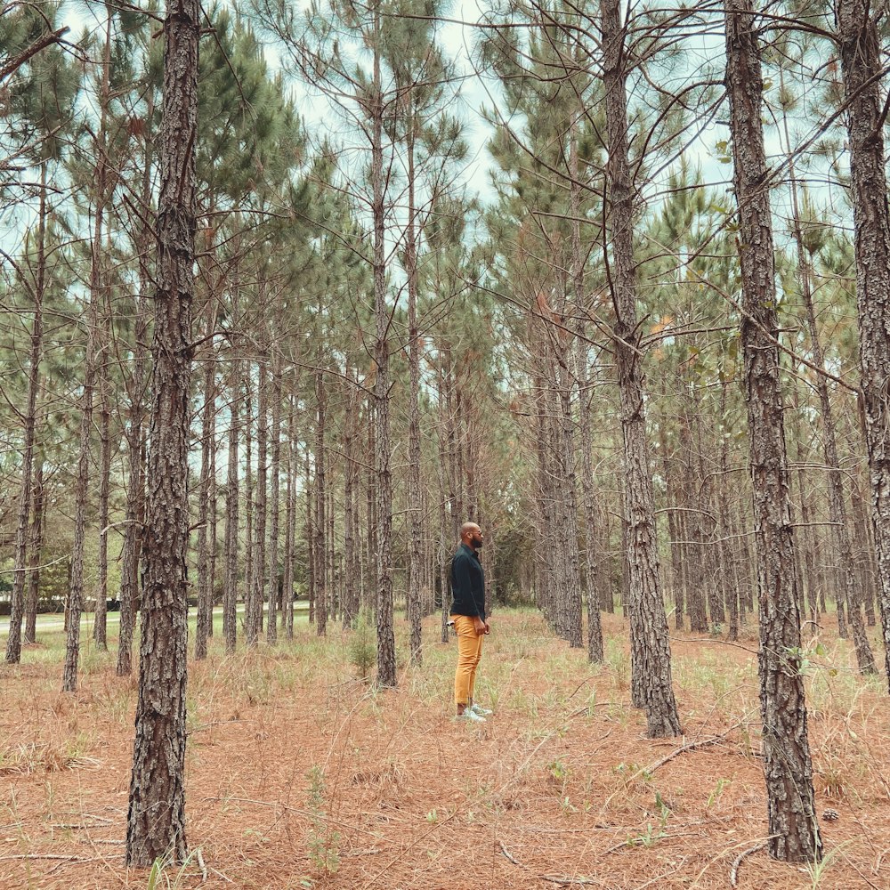 man in black t-shirt and brown pants standing on brown dirt road between trees during