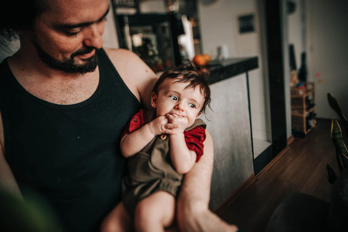 A father sitting close beside his young child, both resting together at home