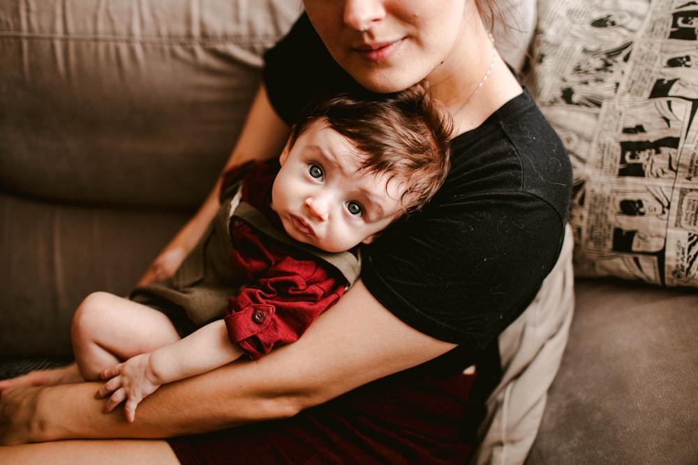 woman in black shirt carrying baby in red dress