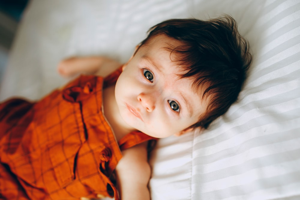 boy in orange and black plaid button up shirt lying on white textile