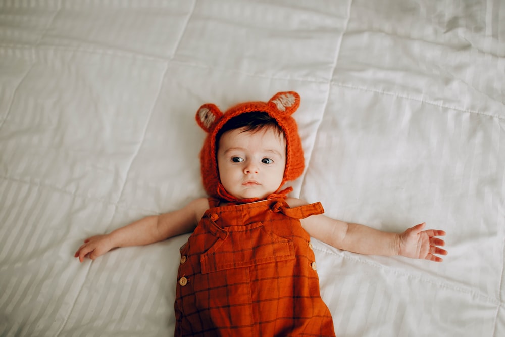 baby in red and black plaid dress lying on white bed