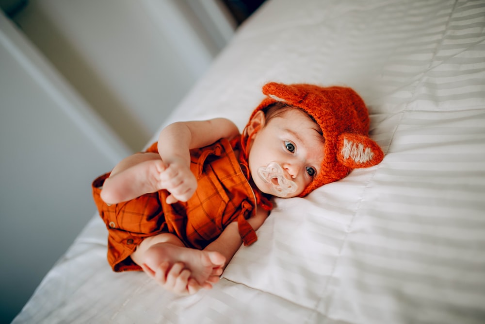 baby in orange knit cap lying on white bed