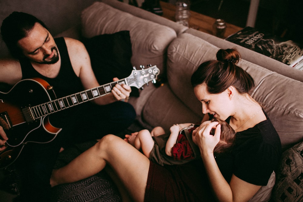 a man and a woman sitting on a couch playing guitar