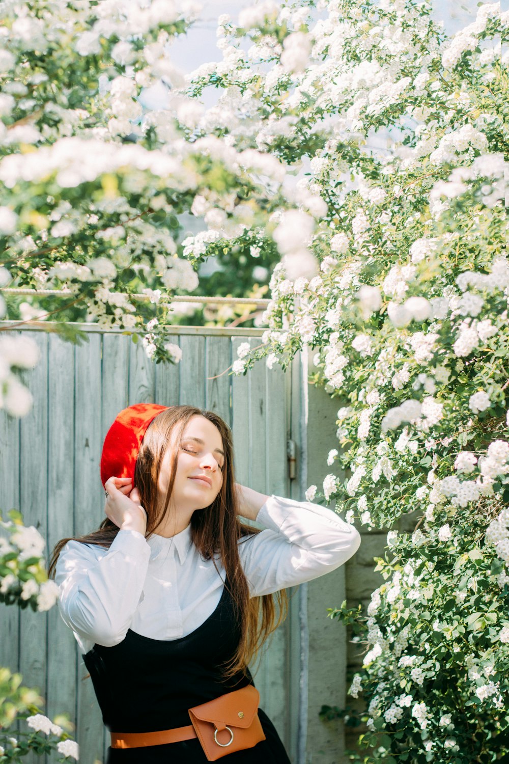 woman in white dress shirt wearing red hat standing beside white flowers
