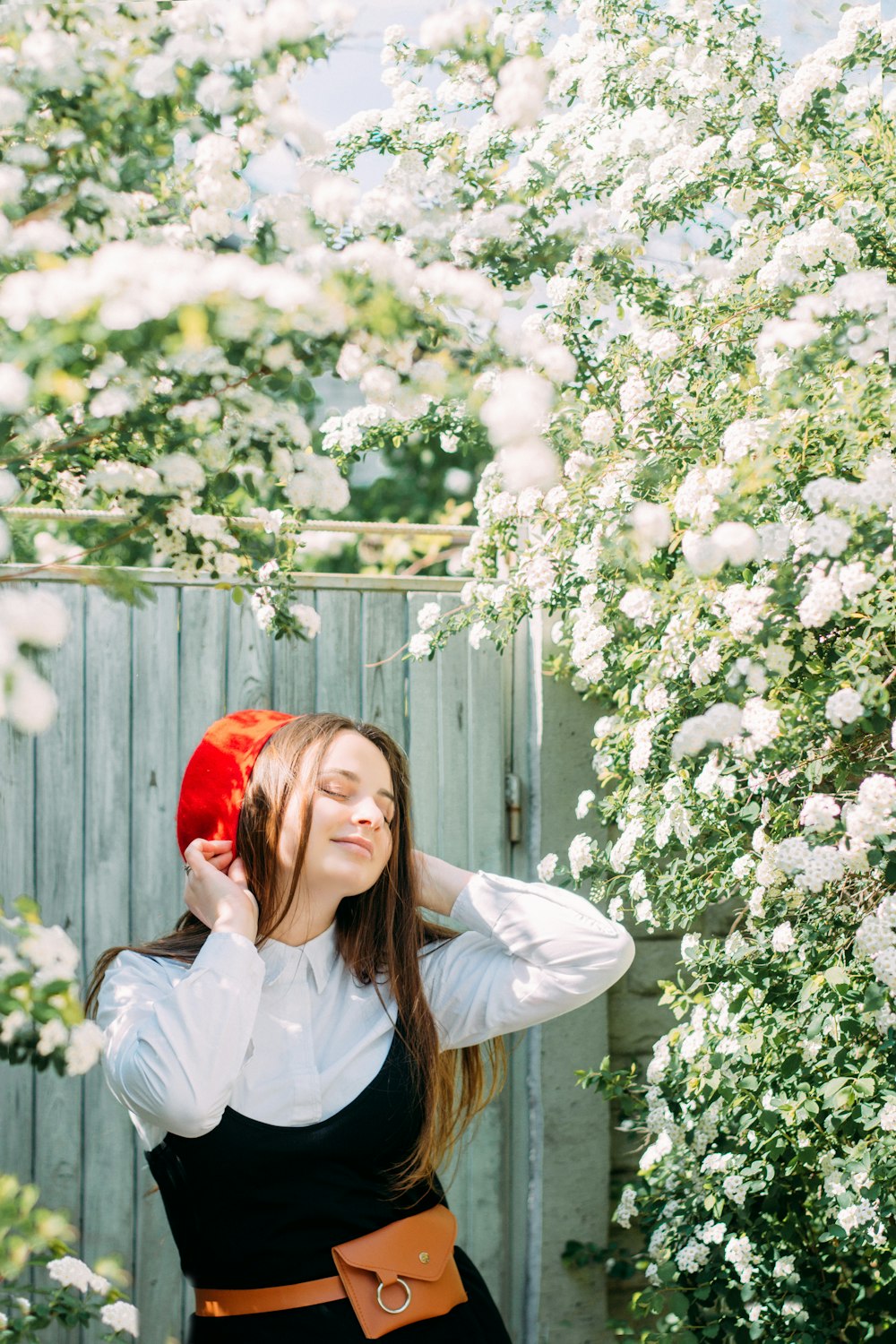 Mujer con camisa de vestir blanca con sombrero rojo de pie junto a flores blancas