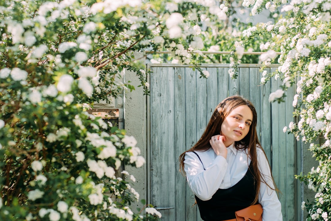 woman in white long sleeve shirt standing beside white flowers