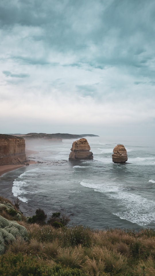 brown rock formation on sea under white clouds during daytime in Port Campbell National Park Australia