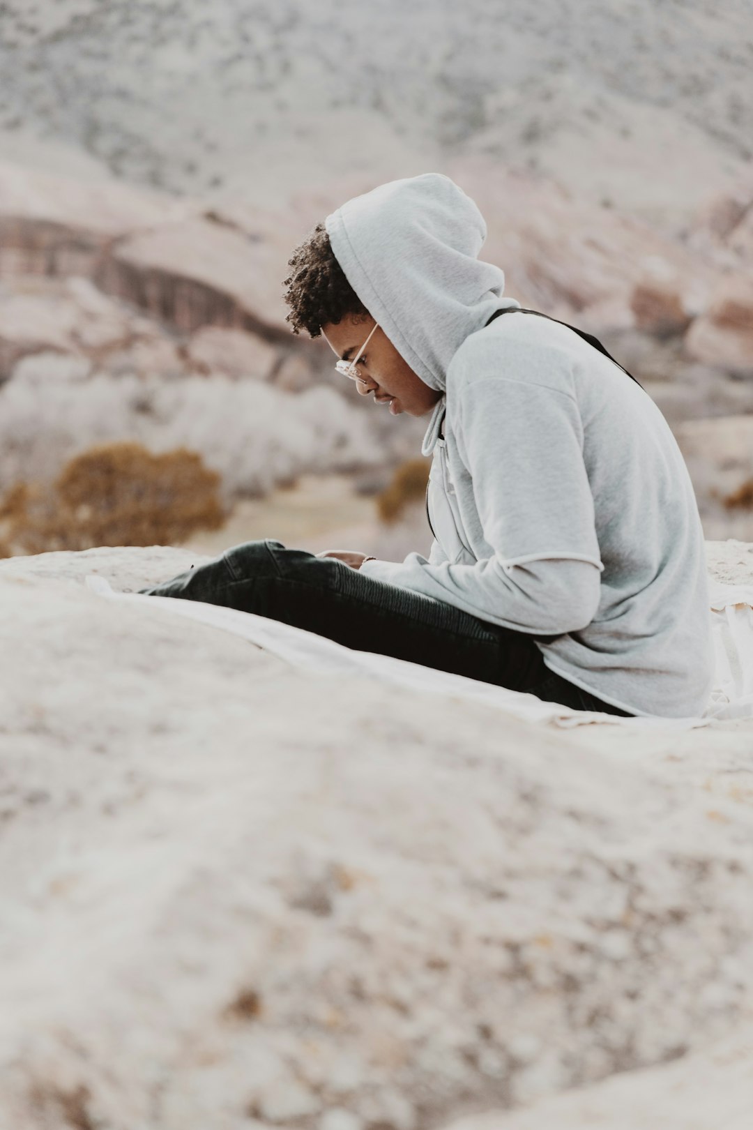 woman in gray hoodie and black pants lying on white rock during daytime