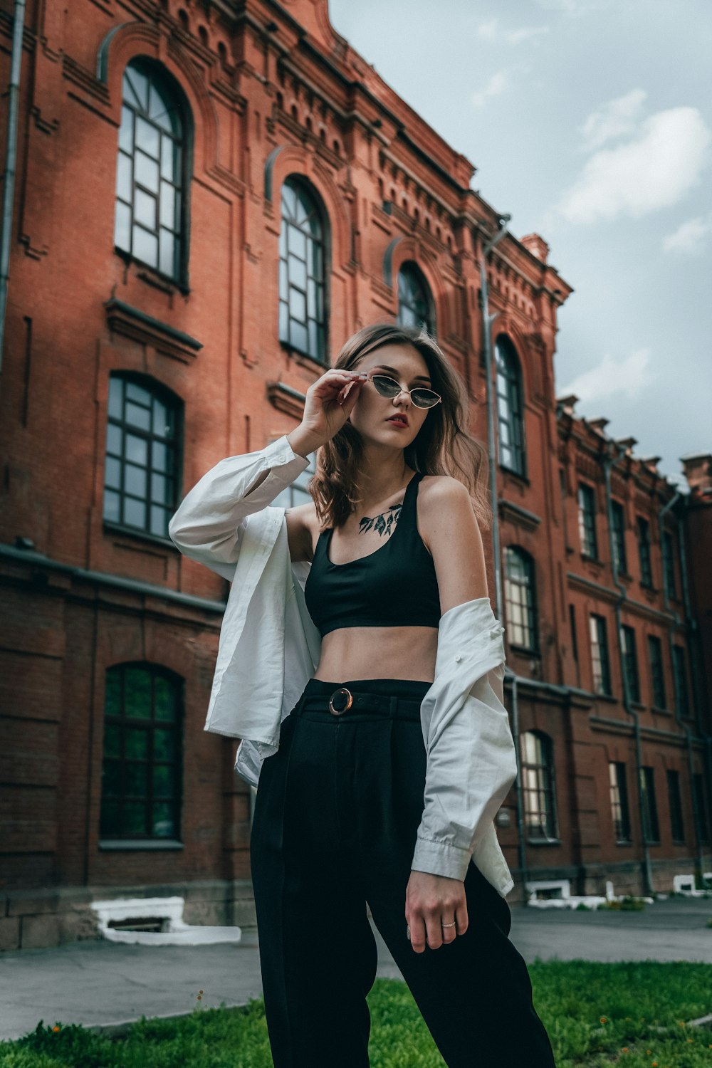 woman in black spaghetti strap top and white cardigan standing near brown concrete building during daytime