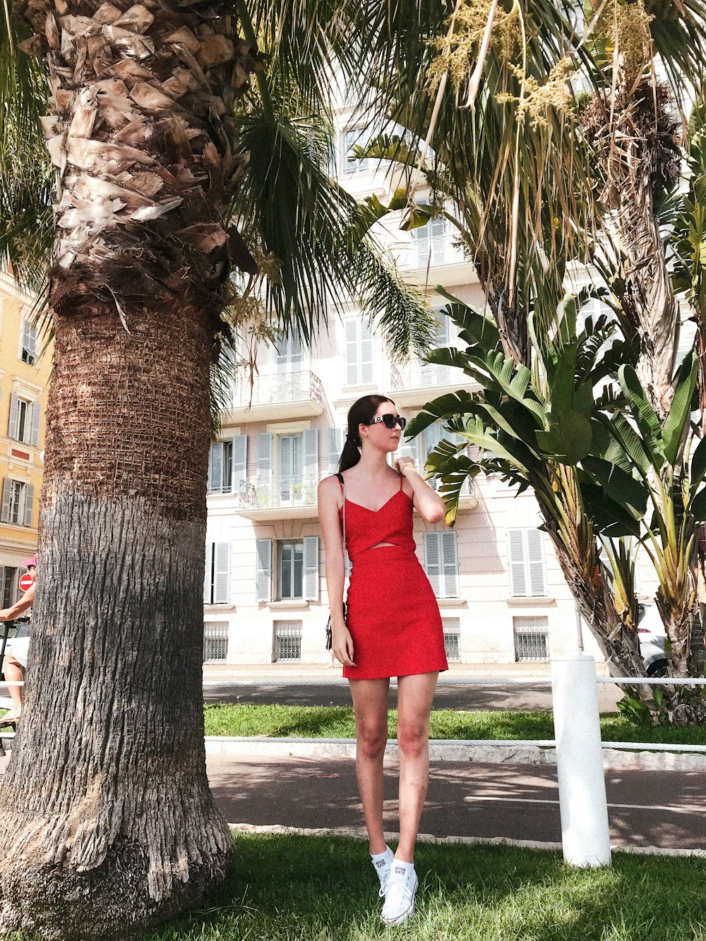 woman in red sleeveless dress standing on gray concrete pathway near palm tree during daytime