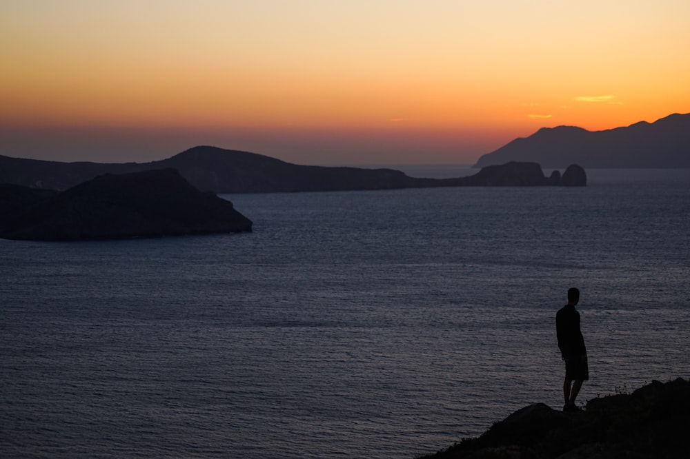 silhouette of mountain beside body of water during sunset