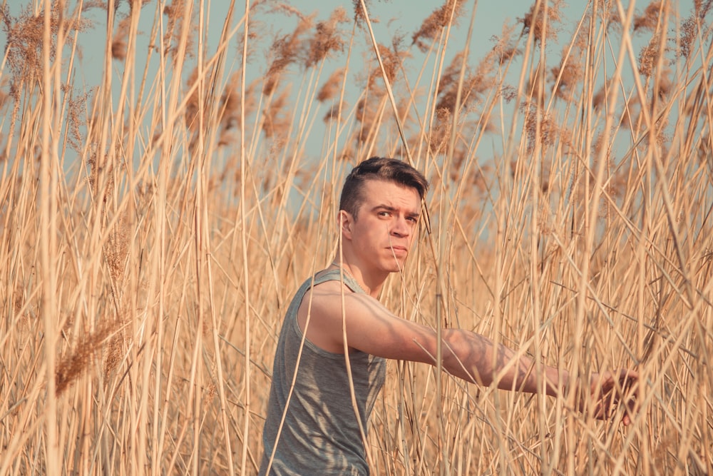 man in grey tank top standing on brown grass field during daytime