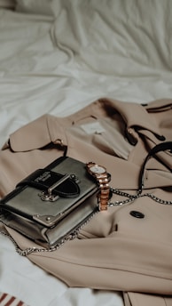 A sleek, minimalistic flat lay of a beige trench coat paired with gold accessories on a white background.
