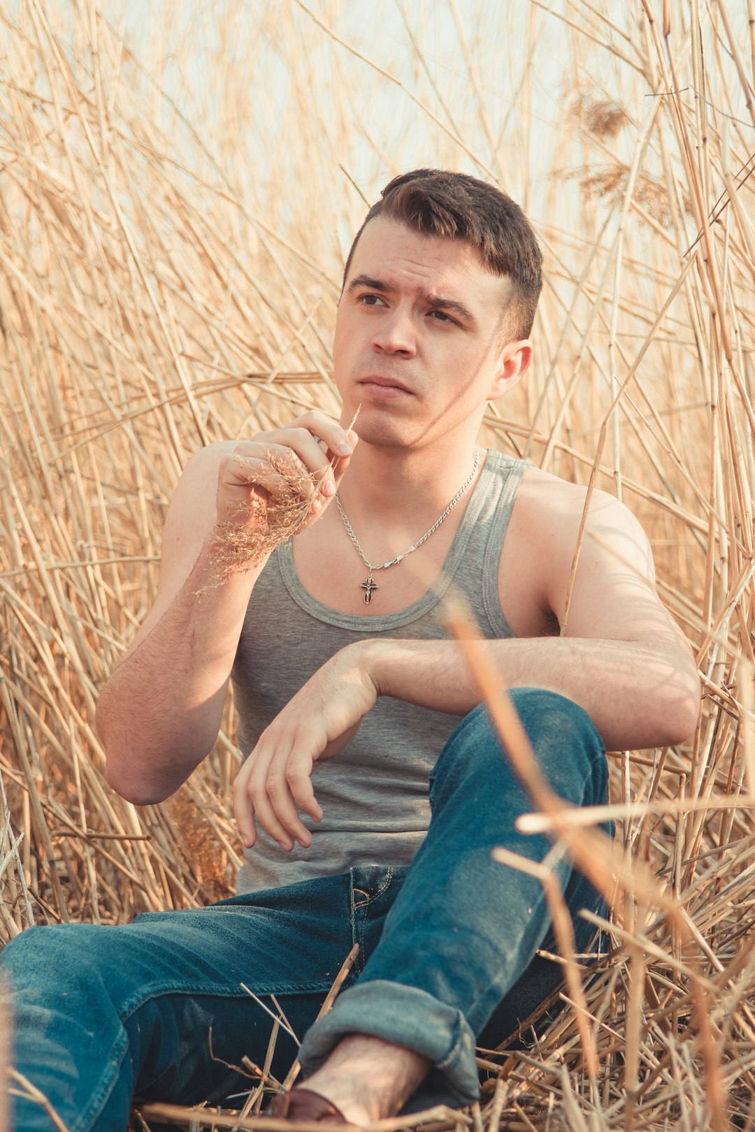 man in gray tank top and blue denim jeans sitting on brown grass field during daytime