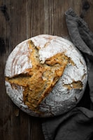 A rustic wooden countertop with a round sourdough loaf cooling on a linen cloth.